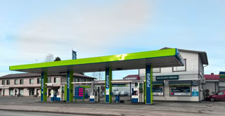 A gas station with a green and blue canopy, multiple fuel pumps, and a convenience store in the background.