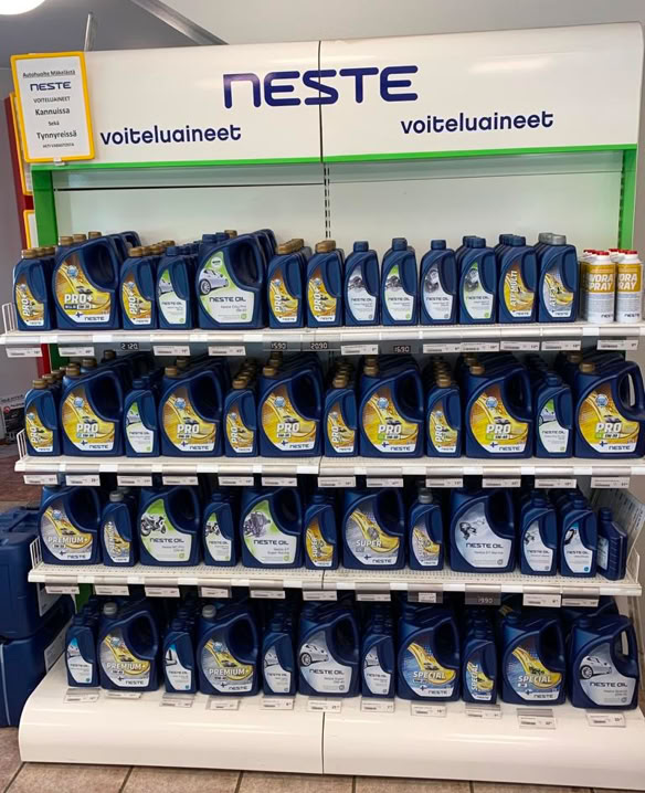 A store shelf displaying multiple rows of blue containers with yellow and white labels, under a sign that reads "NESTE."