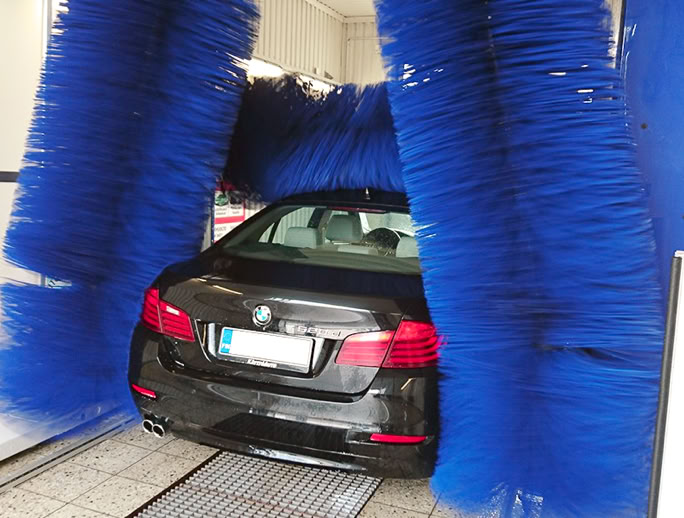 A black car going through a car wash with large blue brushes surrounding it.