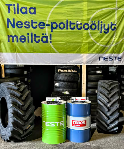 A display of large tires and three barrels, one green and two blue, with a banner above them.